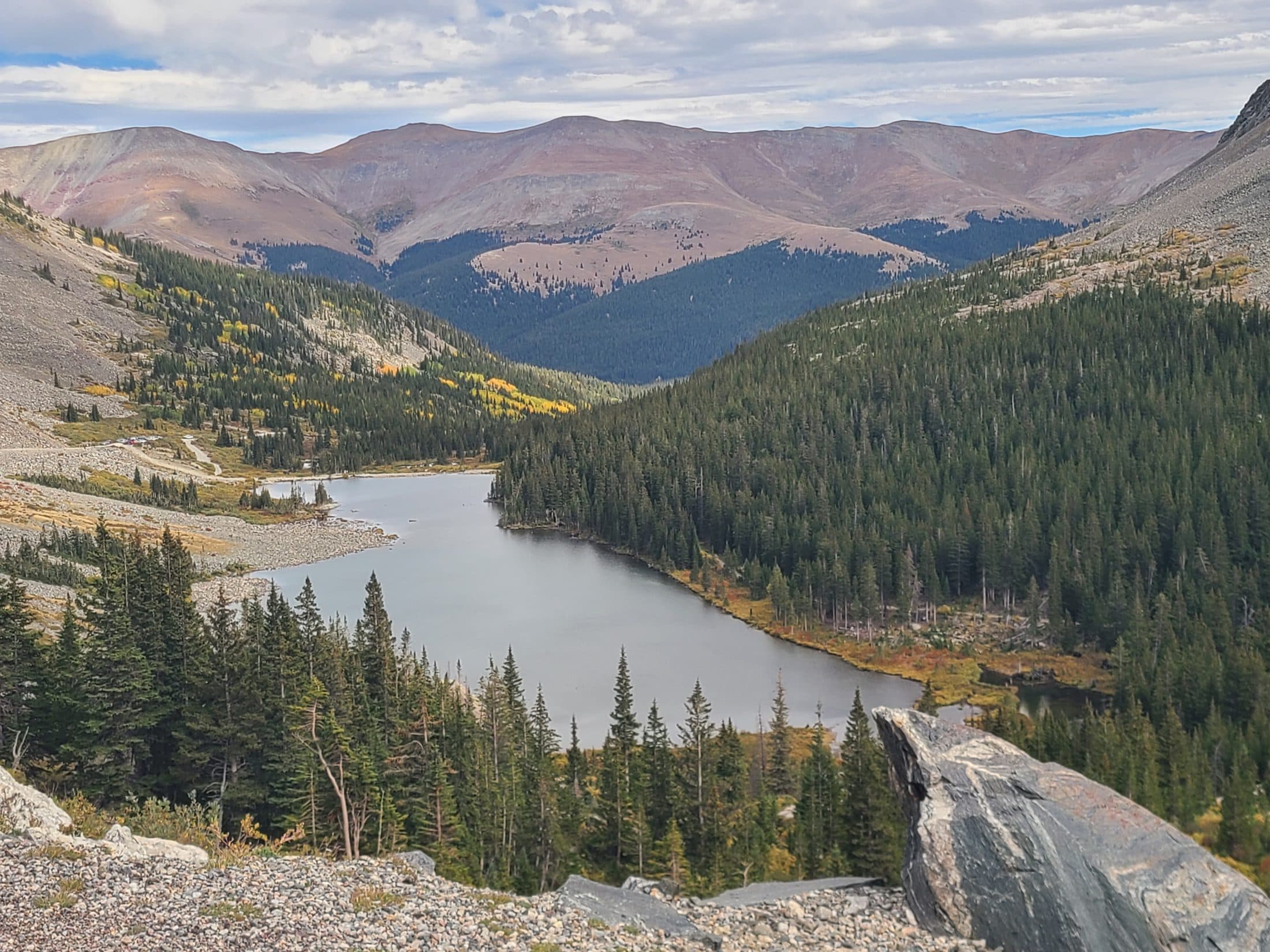A high alpine lake ringed by pines, below bare Colorado peaks.