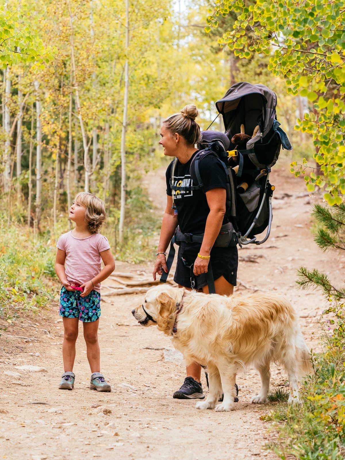 Sarah and Bellamy walking a trail through golden aspens with their dog.