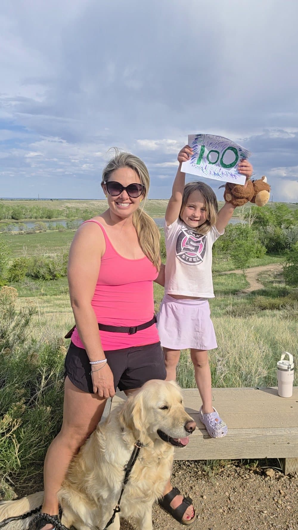 Sarah and Bellamy celebrating with their hundred-hike sign and the dog.