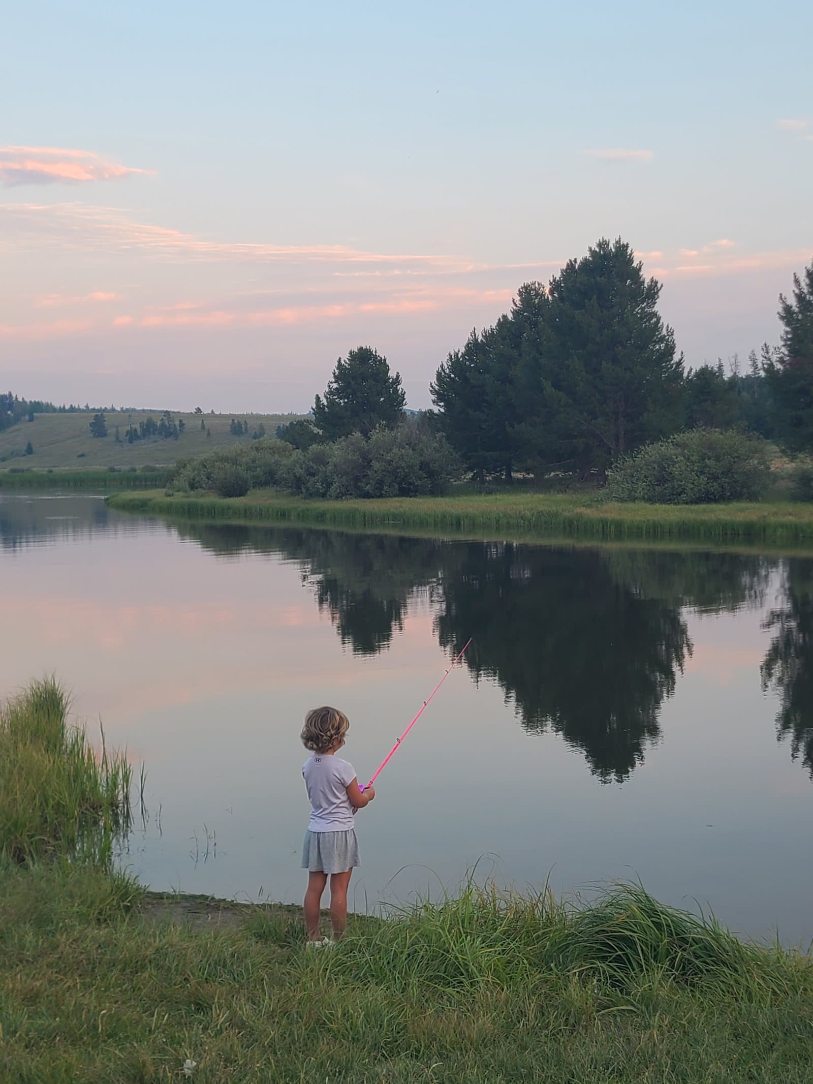 Bellamy fishing at the edge of a still pond as the sun goes down.