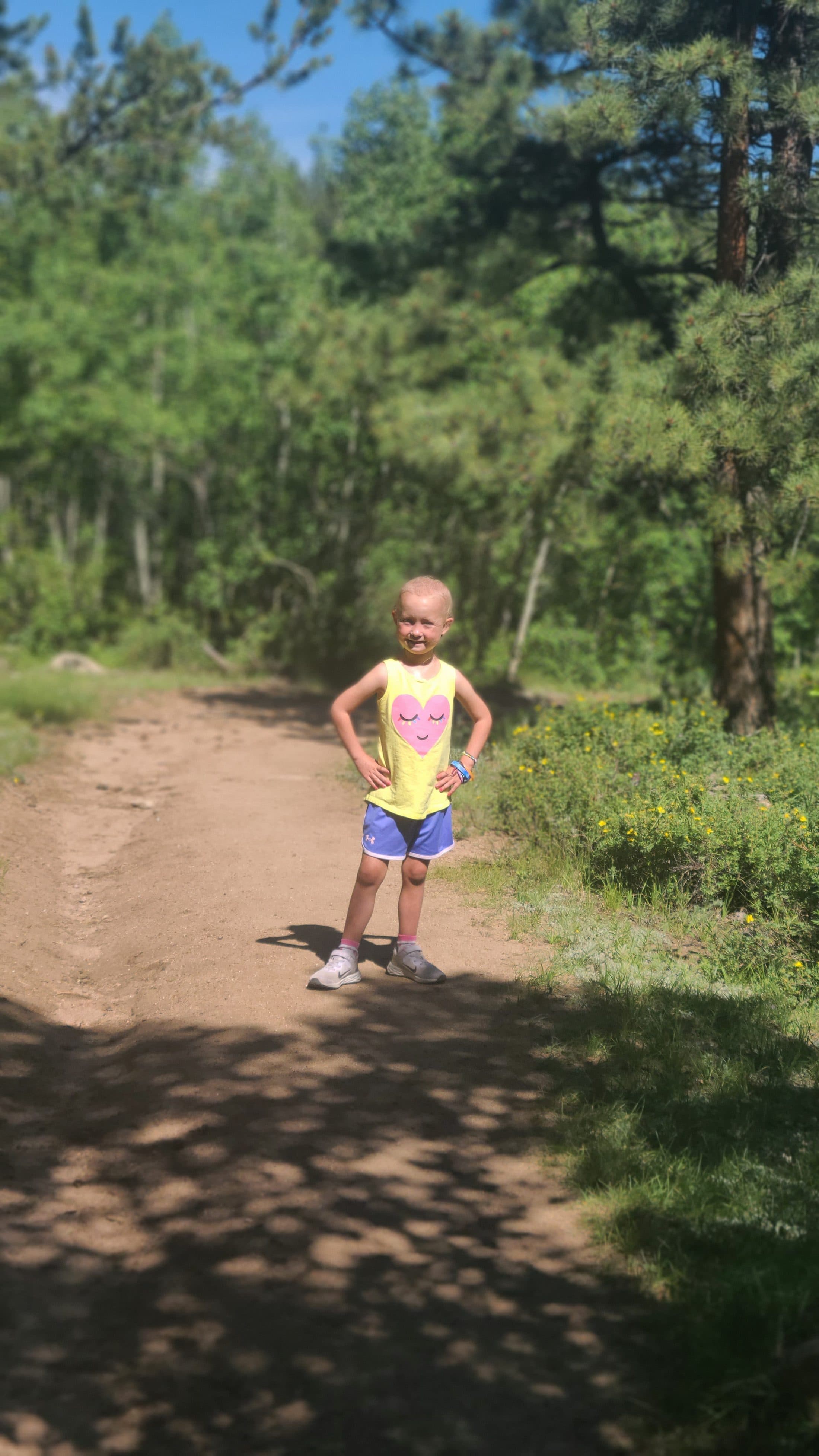 Standing on a forest trail, hands on hips, grinning.