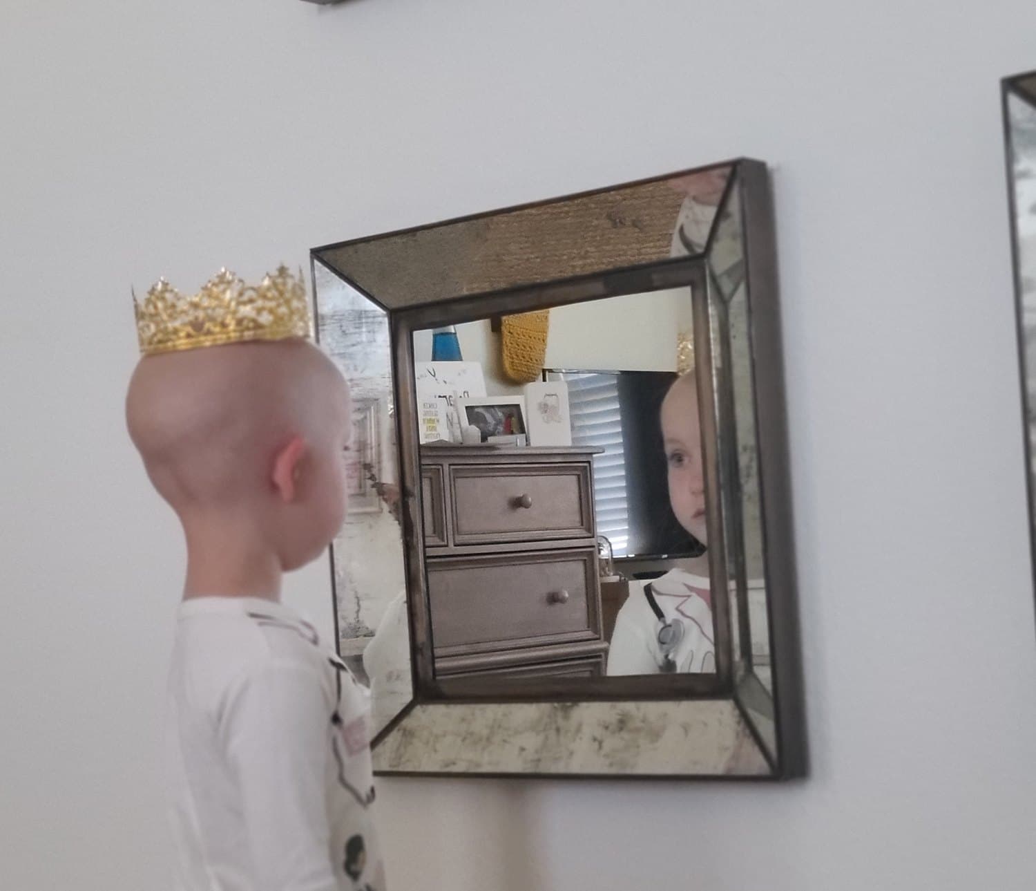 Bellamy in a gold paper crown, in profile, looking at her own reflection in a mirror during treatment.