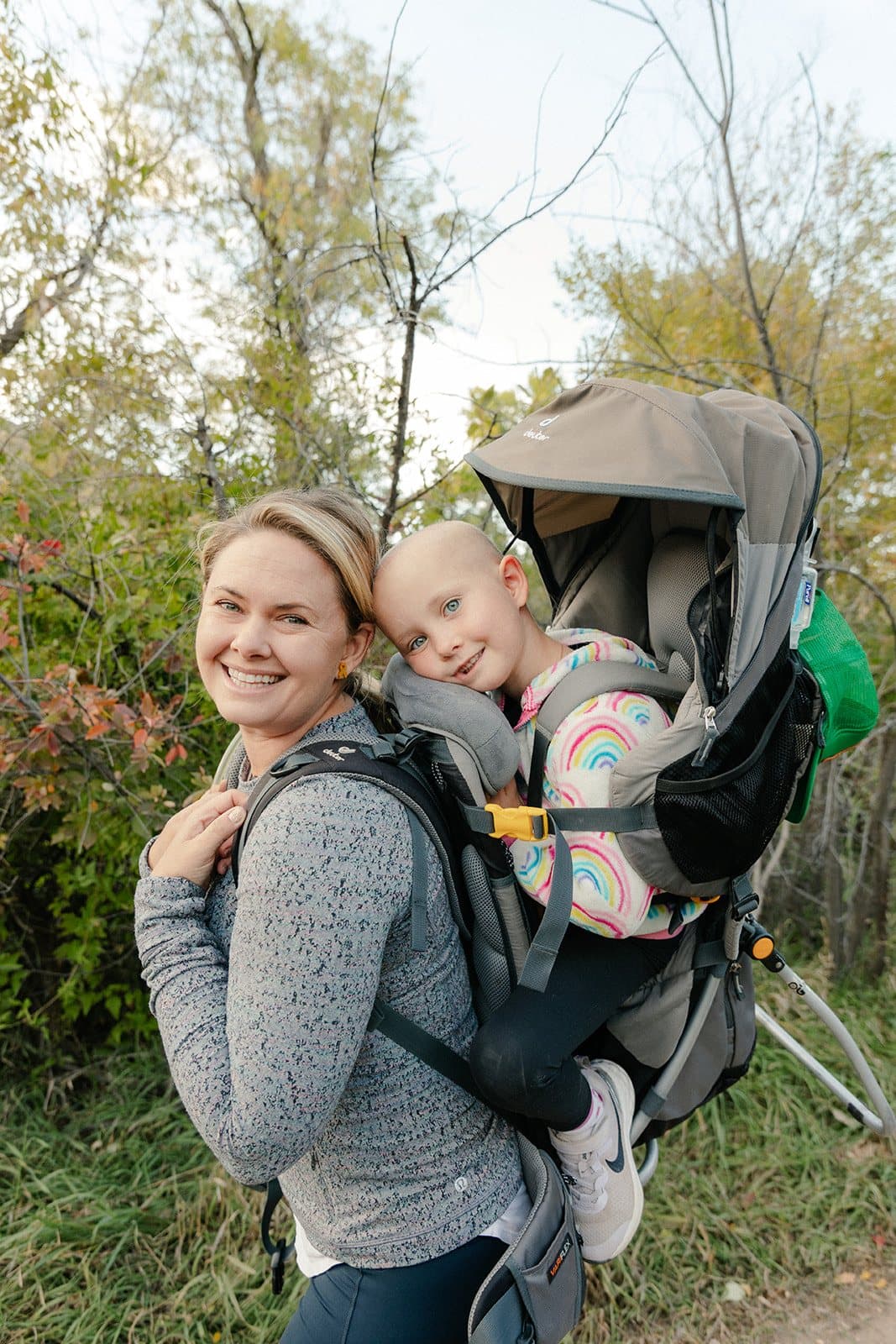 Sarah smiling with Bellamy riding in a hiking carrier on her back.