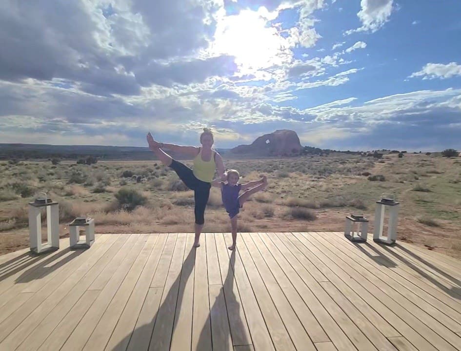Sarah and Bellamy side by side in dancer's pose on a wooden deck, red rock desert and a wide open sky behind them.